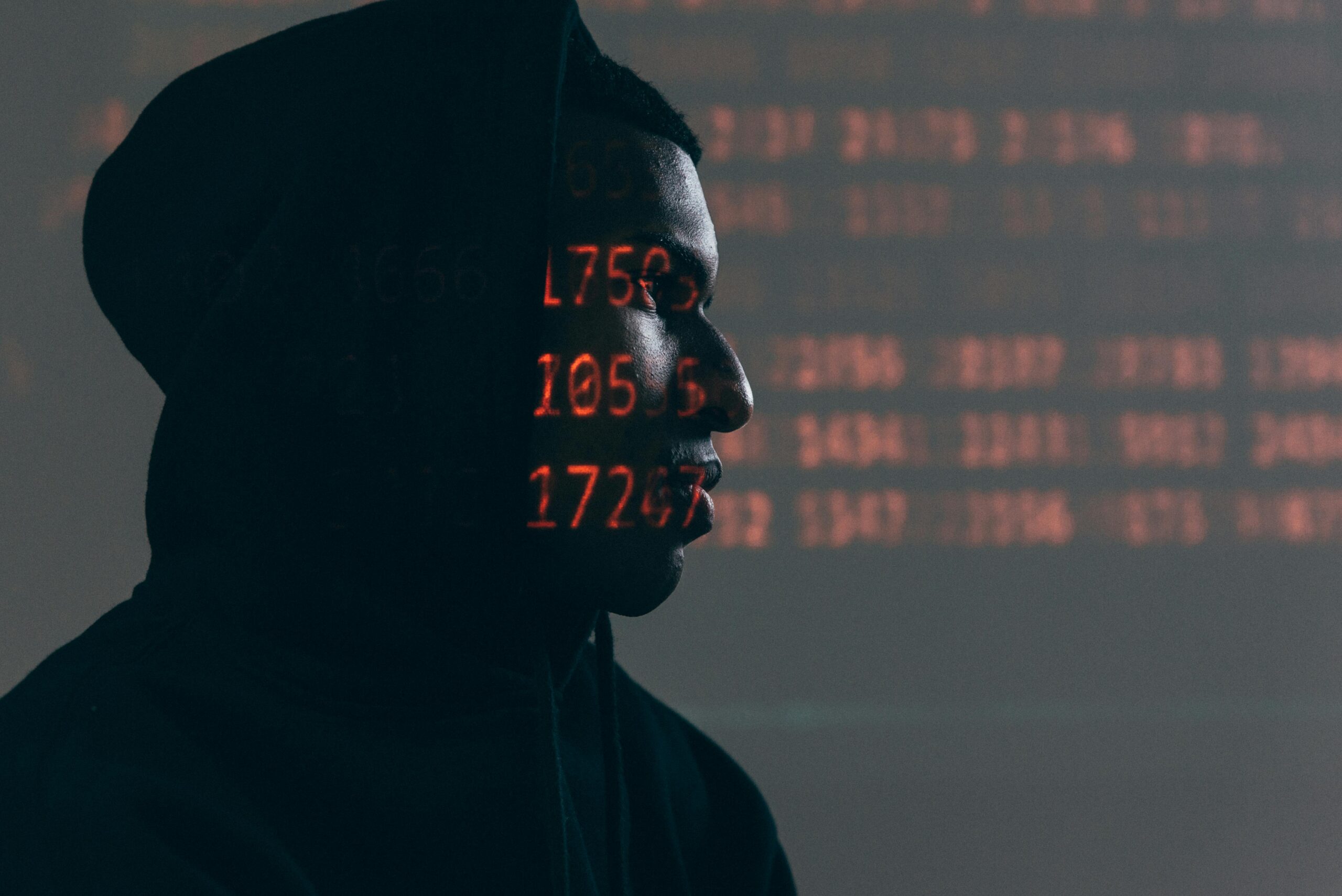pexels-photo-5952651-5952651 Side profile of a man in a hoodie, surrounded by red code, depicting cybersecurity theme.